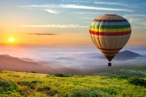 Big hot air baloon over idyllic landscape with green grass covered morning mountains with distant